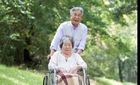 Asian man pushing his wife in a wheelchair